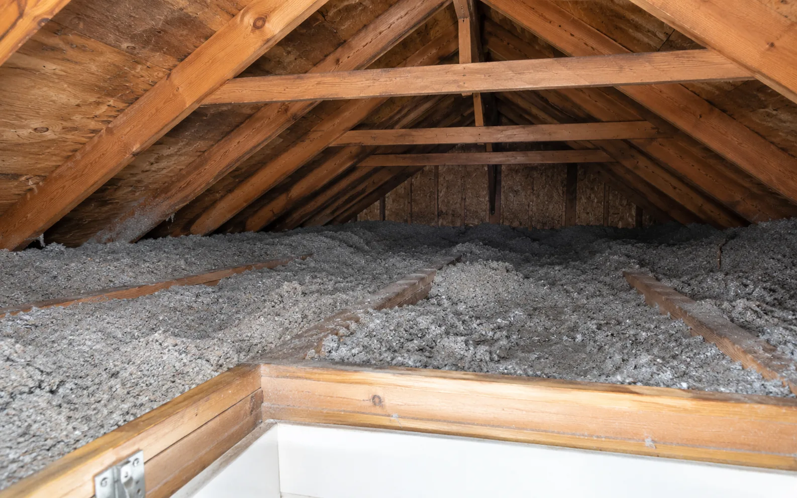 Existing grey insulation and timber framing viewed from an attic access opening.