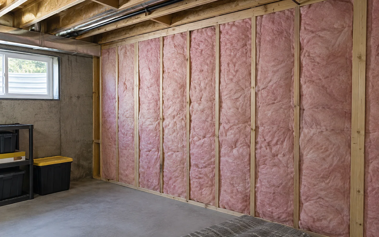 Insulated wall cavities in an unfinished basement room.