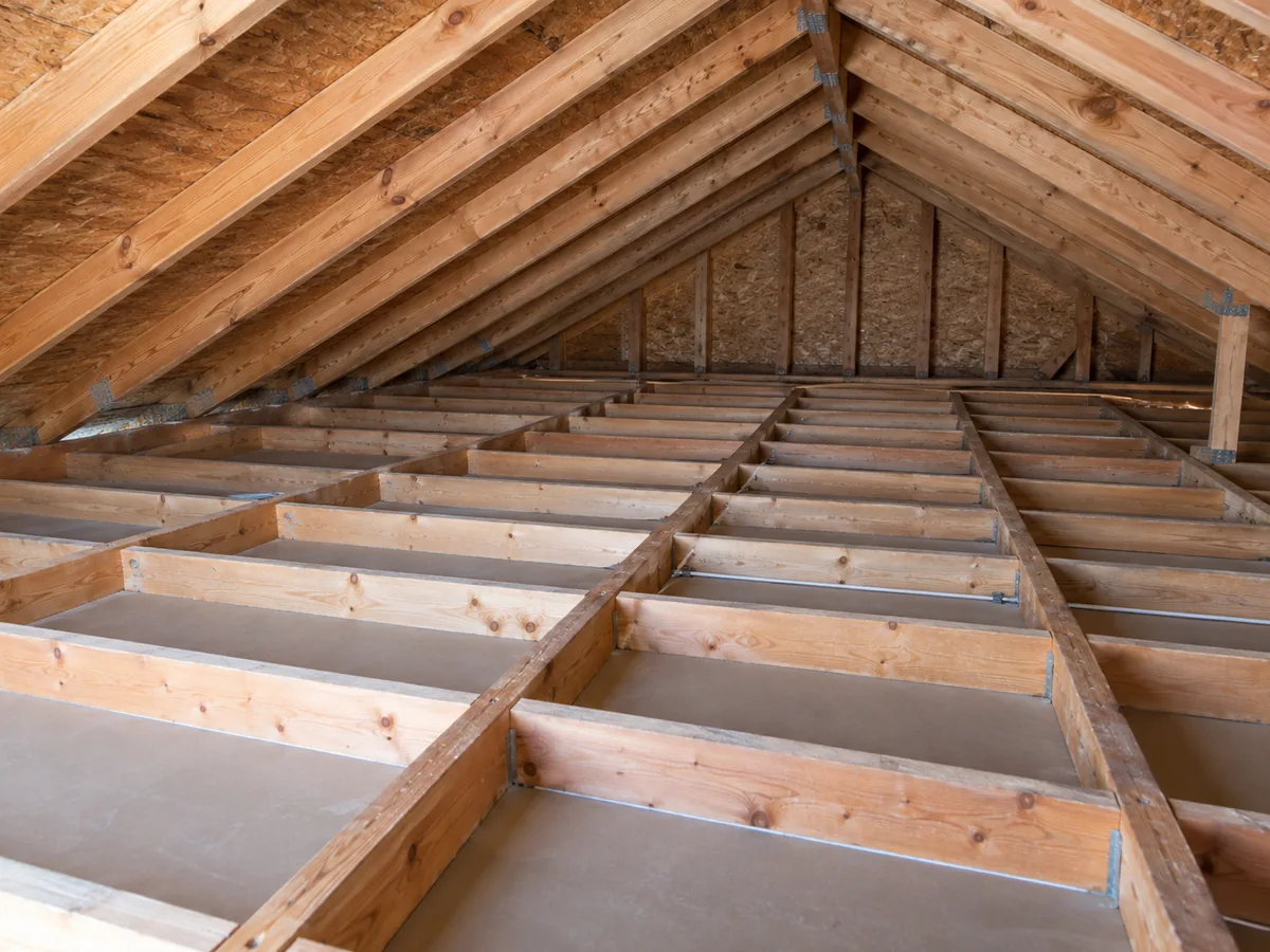 Exposed ceiling joists and the back of ceiling boards in a cleared attic work area.