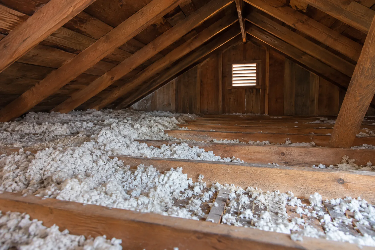 Uneven loose-fill coverage and exposed timber across an existing attic floor.